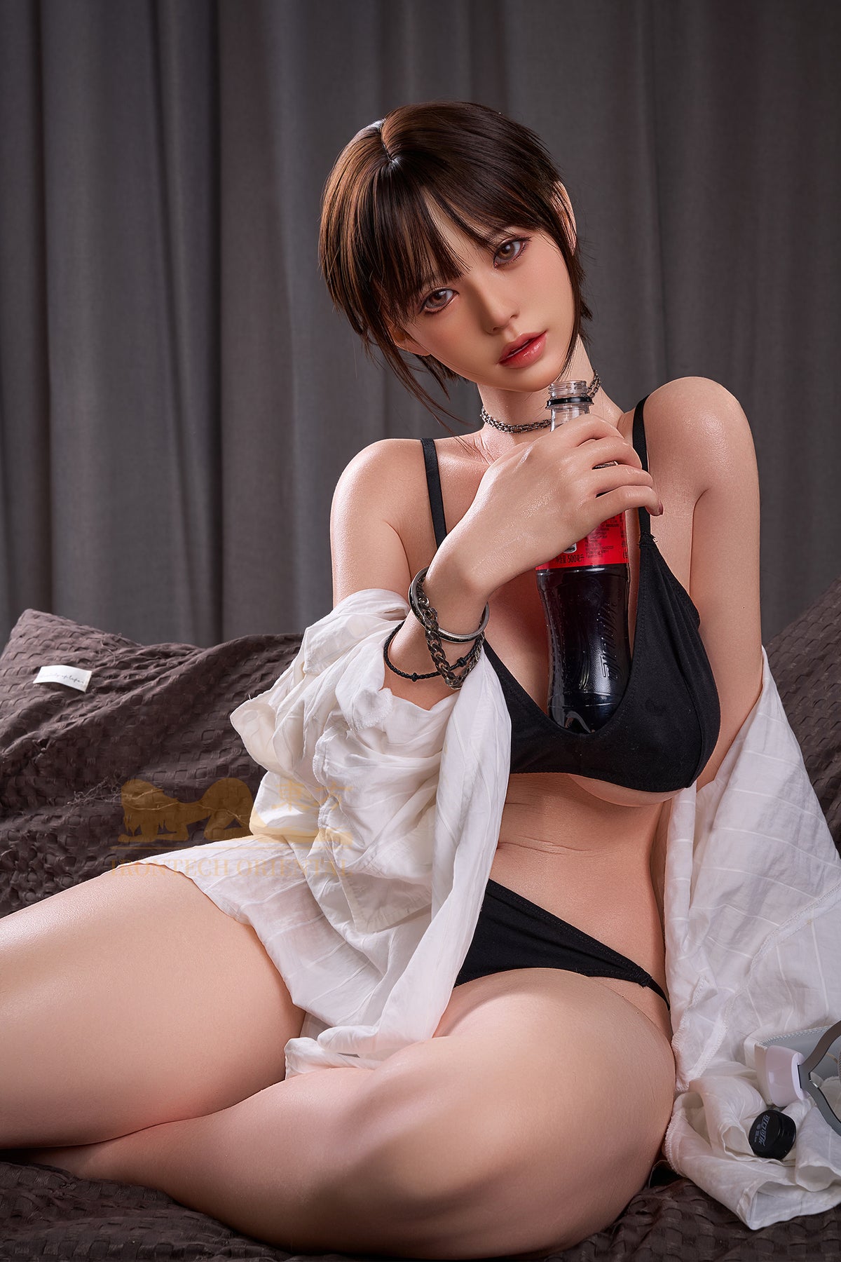 The Irontech Doll 153 cm E Oriental Series Silicone – Yuna V3 in a relaxed pose on a textured brown surface, holding a bottled beverage and wearing a silver choker necklace.