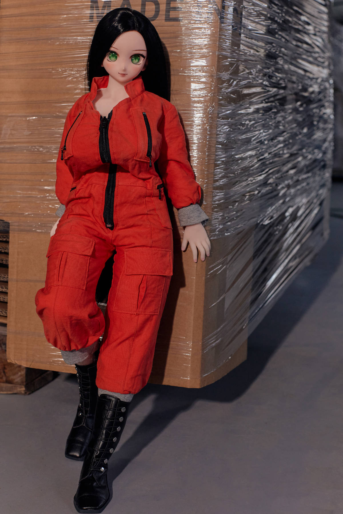 CLIMAX DOLL Mini J60cm P Hybrid - Rina (Cinnamon) standing pose in the zipped red coverall and black boots, leaning against stacked boxes