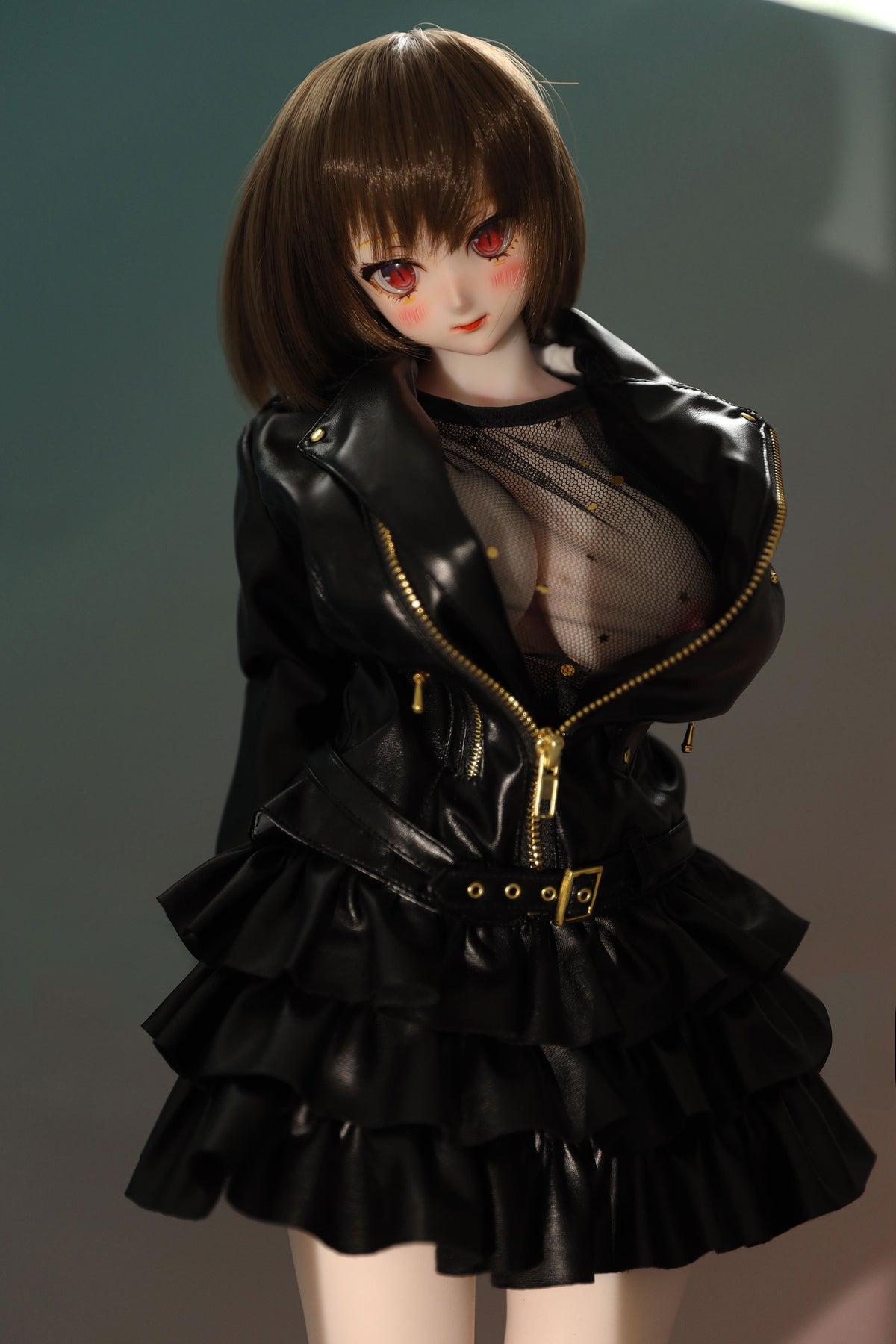 CLIMAX DOLL Mini J60cm P Hybrid - Zella (White) - Front-facing standing portrait with a short brown bob, red-brown anime eyes and a sweet, calm expression, in a glossy black ruffled jacket-dress with gold zipper, teal-green gradient backdrop.