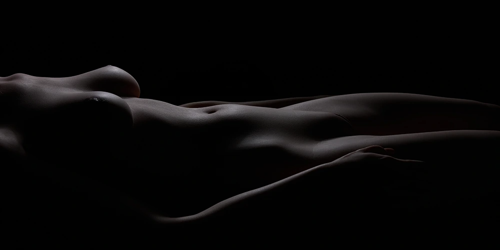 Silhouette of a lifelike female body lying in low light, highlighting realistic curves and contours.