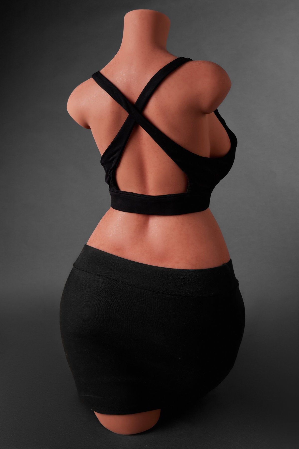 A back view of the CLIMAX DOLL - ULW 883# Silicone Torso (Black) dressed in a black mini skirt and a top featuring a crisscross back strap design.