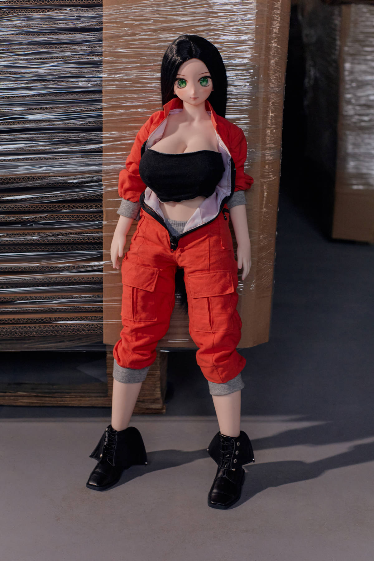 CLIMAX DOLL Mini J60cm P Hybrid - Rina (Cinnamon) standing pose with the red jumpsuit open at the front over a black bandeau top, black boots, warehouse backdrop