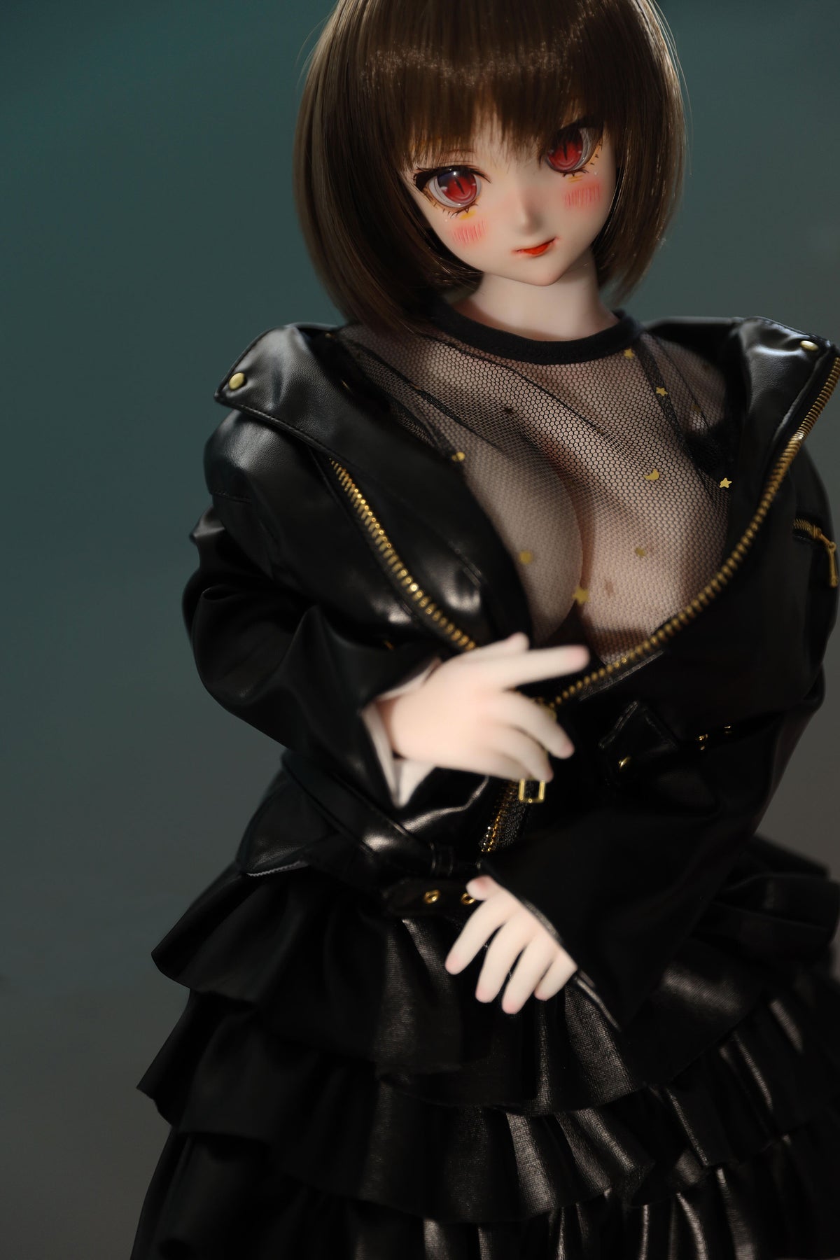 CLIMAX DOLL Mini J60cm P Hybrid - Zella (White) - Waist-up close-up with the black ruffled jacket worn open over a sheer mesh top, one hand resting near her chest, soft demure expression, teal-green background.