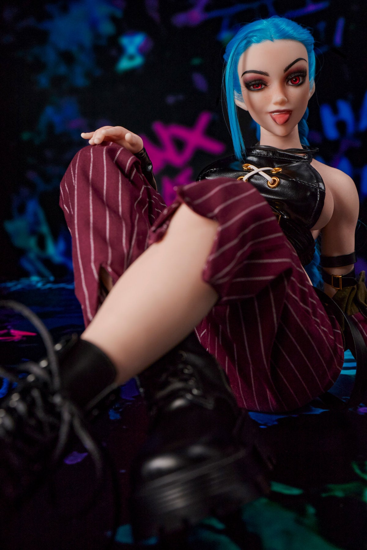 CLIMAX DOLL Mini Si70cm MO Silicone - Jetta (Cinnamon) three-quarter view in black crop top and red plaid pants with raised hand pose, blue hair, dark bokeh background
