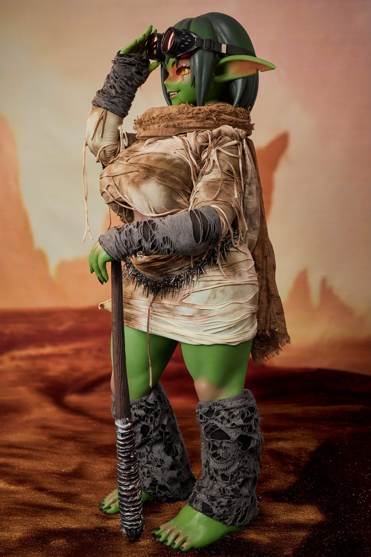 CLIMAX DOLL ULW SiF120 cm Silicone - Barza (Green) front view in tattered tan wrap with bound arms pose, short green hair, desert red background

