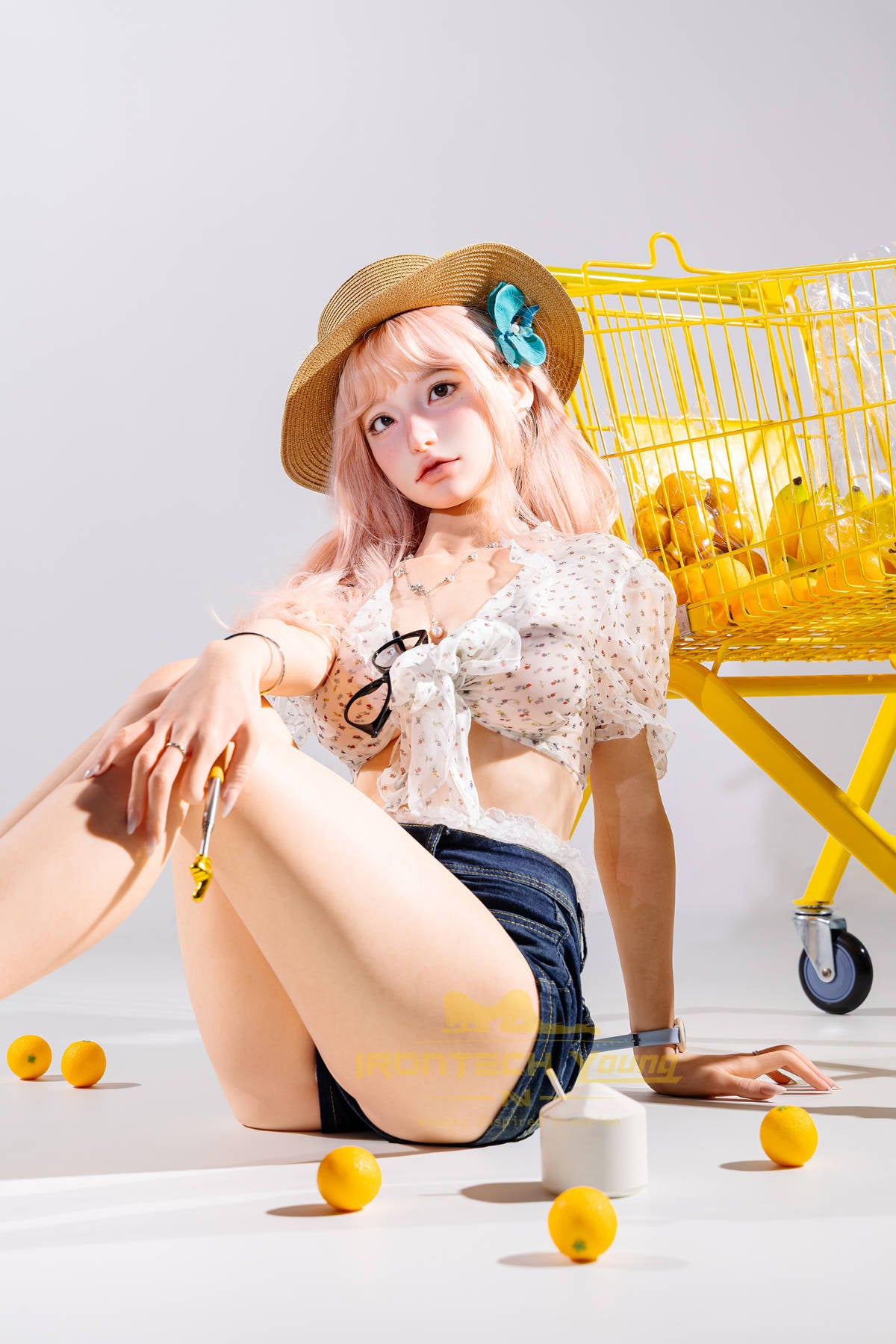 Irontech Doll 166 cm 2.0 Young Series E Silicone - Mio seated pose in a white crop top and denim shorts, yellow prop styling in the background