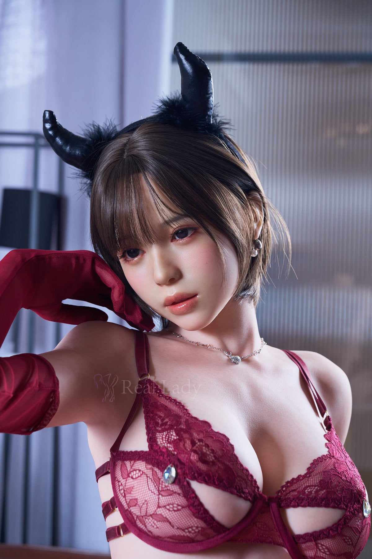 RealLady 159cm H Silicone - Alara – Seated pose, black horns headpiece, red lace bra and sheer gloves, dark bob hair, softly lit indoor backdrop.
