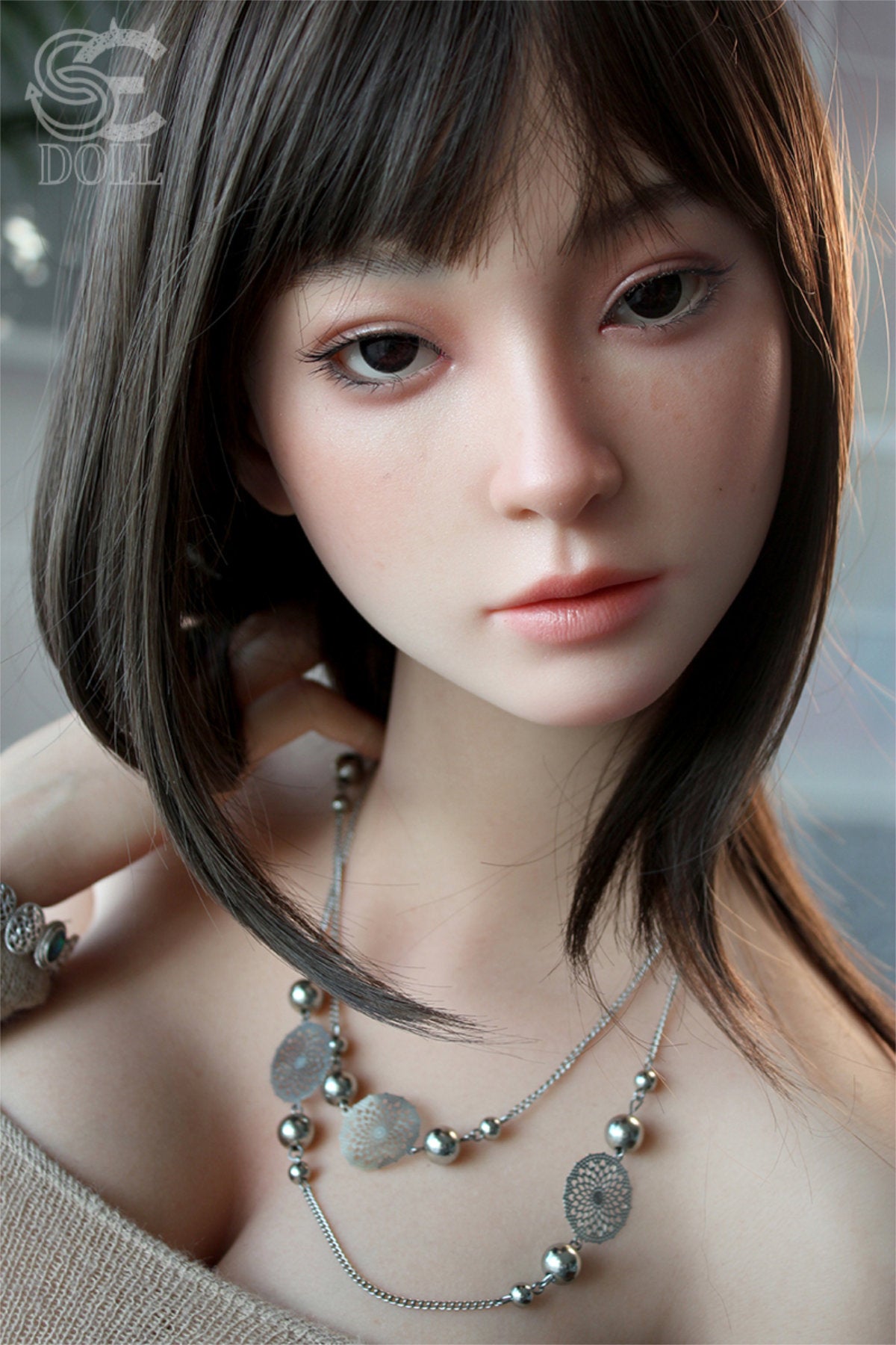 SEDOLL T161cm C Aya Series Silicone - Miori.C – Close-up pose wearing a layered pendant necklace, white lace-trim top slightly pulled down, dark hair with bangs falling just above the eyes, soft neutral backdrop.