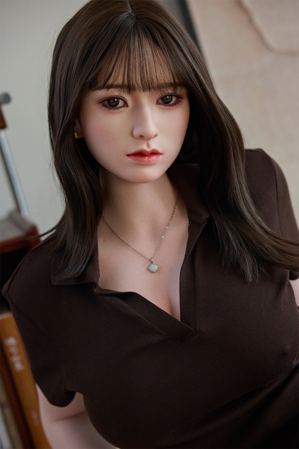 Starpery 154cm E - Yuan – Close-up seated pose, deep brown V-neck short-sleeve top with delicate pendant necklace, straight-cut dark bangs framing the face with hair falling past the shoulders, warm wooden interior backdrop.
