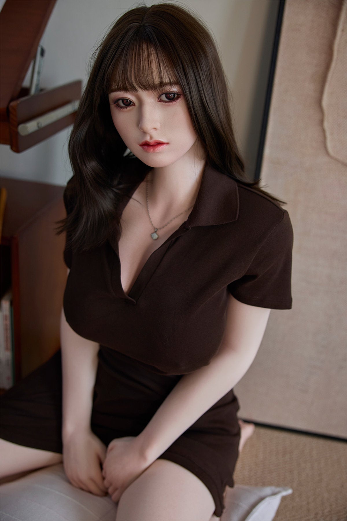 Starpery 154cm E - Yuan – Seated pose leaning forward, brown V-neck top open at the collar revealing the chest, dark straight bangs framing the face, warm interior backdrop.