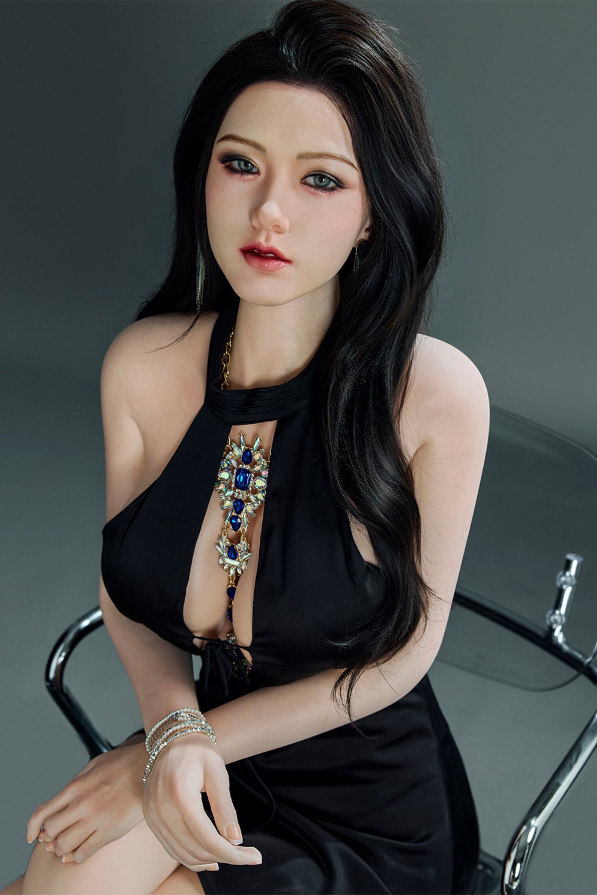 Starpery 171cm D - Jin V2 – Seated pose on a stool, black halter dress with a plunging cutout neckline and beaded strap accents, dark wavy hair draped over one shoulder, moody dark studio backdrop.