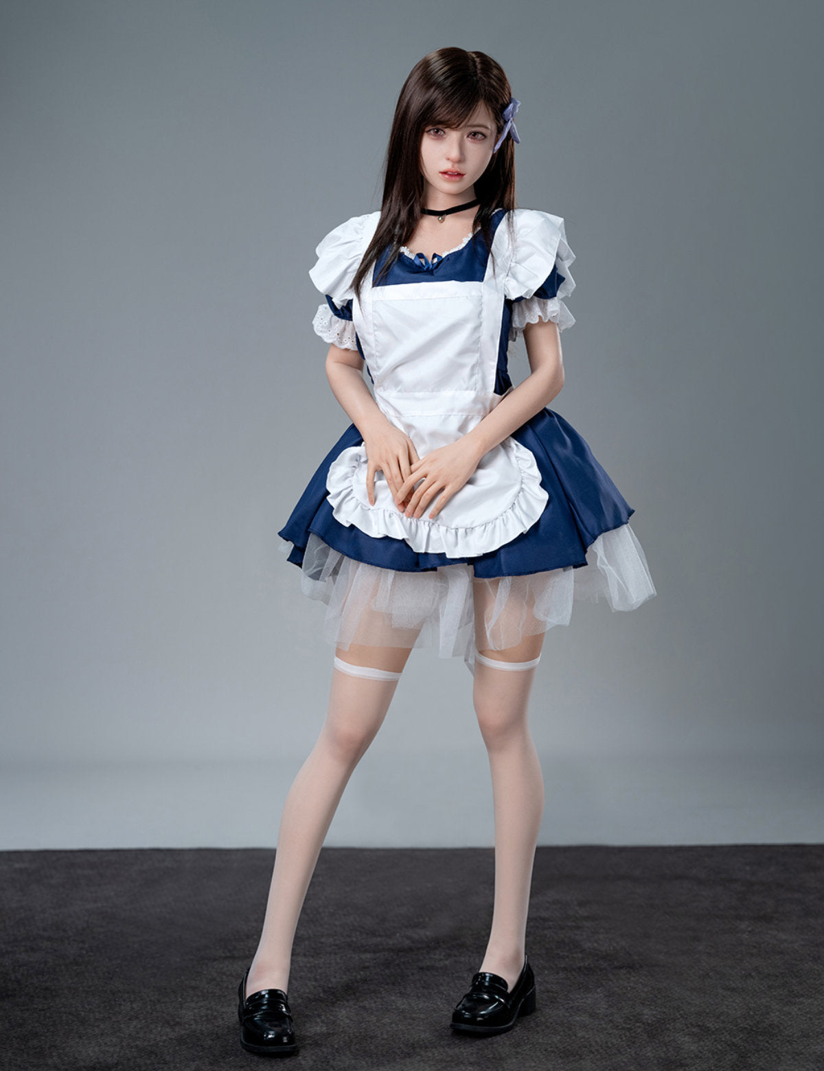 Full-body standing front view of the Koharu doll in a maid costume and white thigh-high stockings against a plain grey studio backdrop.