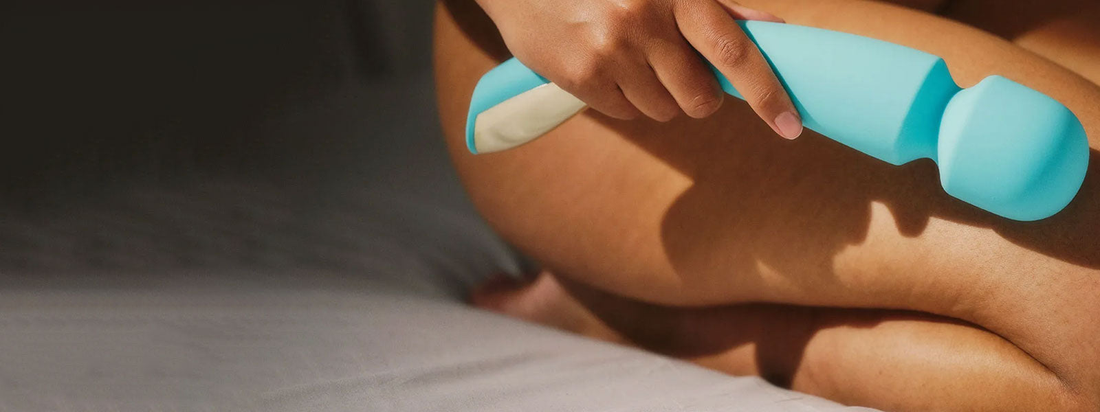 Person using a teal and white handheld wand vibrator on her arm.