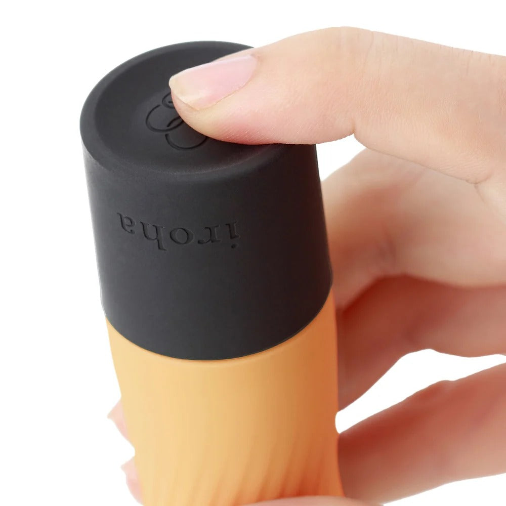 A close-up of a hand holding a cylindrical bottle with a matte black top and a peach-orange lower body. 